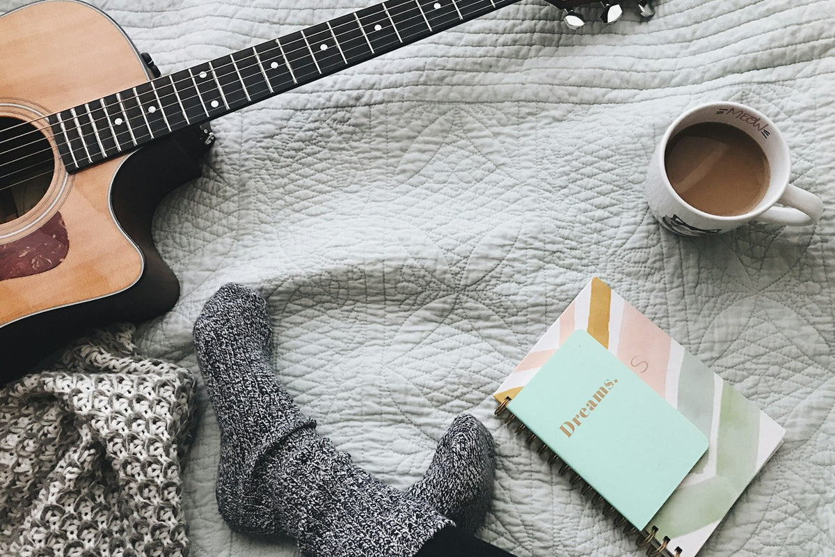 Acoustic guitar, notebook and coffee on a cozy blanket, ready for songwriting