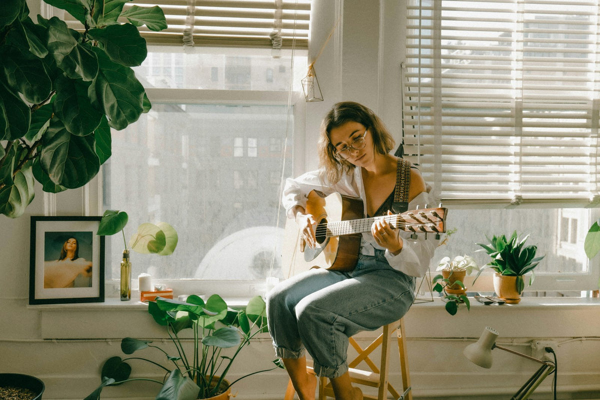 Woman playing acoustic guitar by a sunny window while writing a song