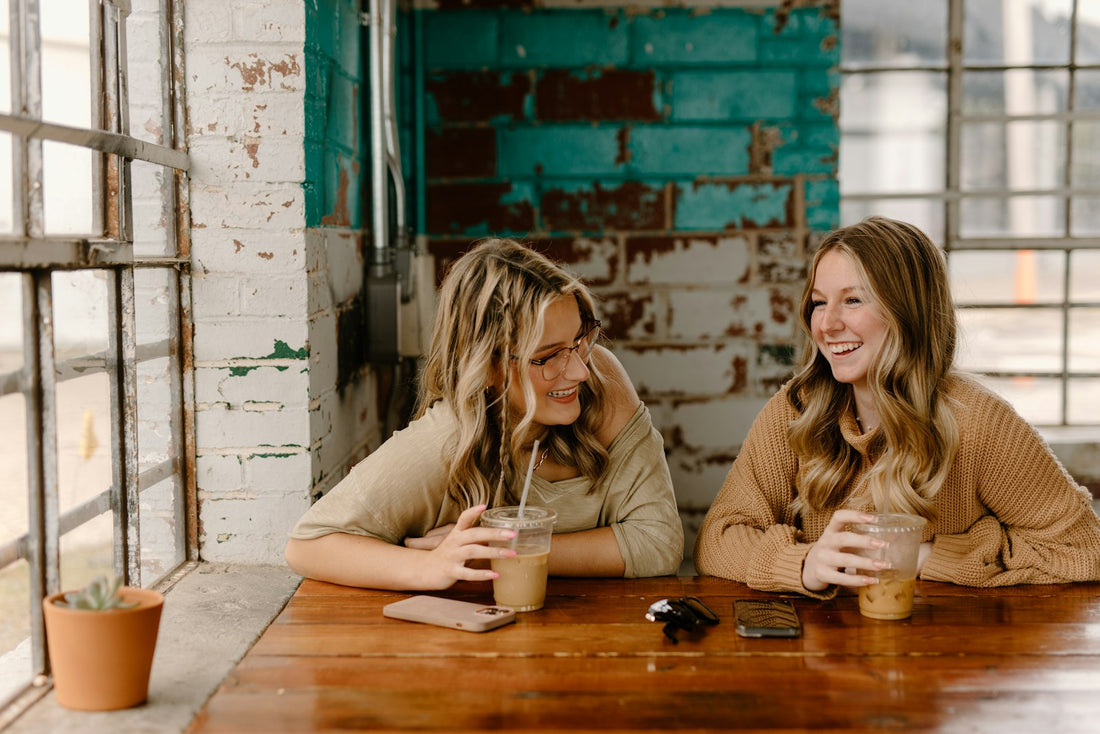 Two best friends laughing together over coffee at a cafe table