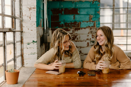Two best friends laughing together over coffee at a cafe table